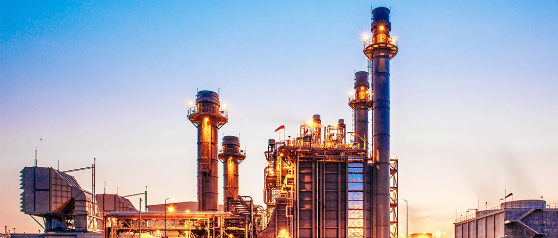A petrochemical plant glows at dusk, with illuminated towers rising against the evening sky.