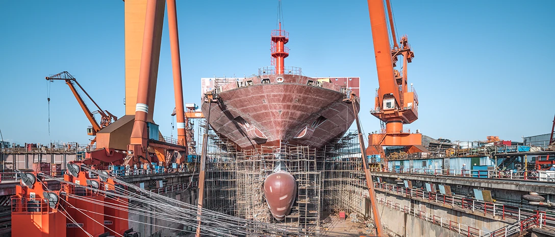 A newly built ship in dry dock surrounded by cranes and scaffolding
