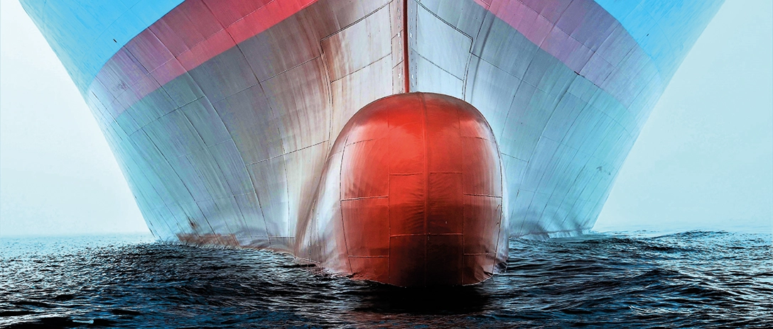 A close-up view of a large ship's bow cutting through the water at sea.