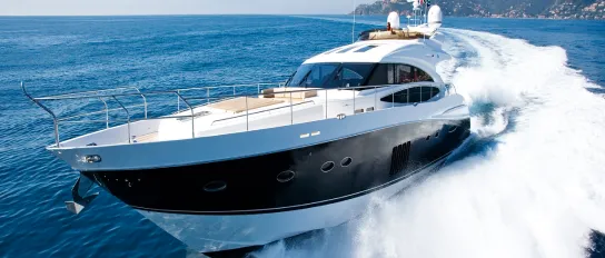 A sleek, modern motor yacht speeds across the water, leaving a trail of white foam behind, with the coastline visible in the distance.