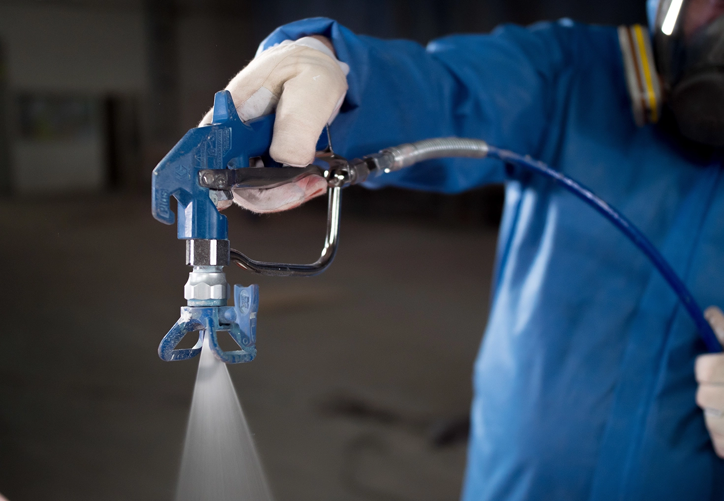 Close-up of a gloved hand operating a spray gun, applying a coating.