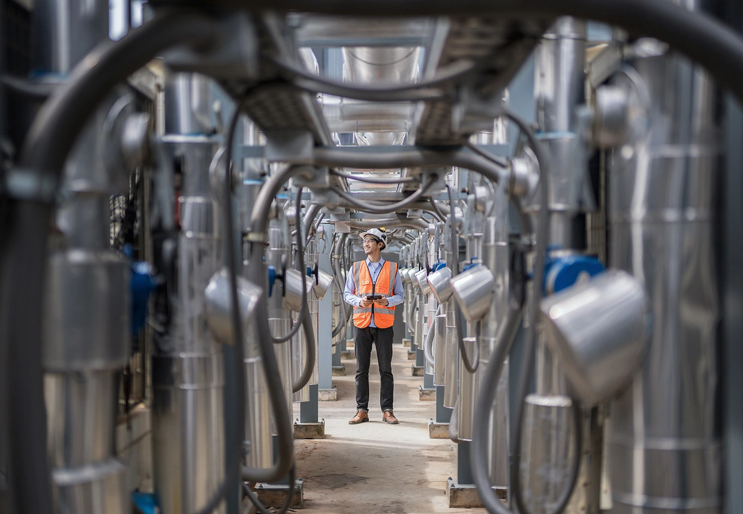 A man stands in a spacious data center, surrounded by large pipes and equipment, indicating a technical environment.