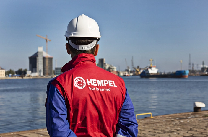 A Hempel's coating advisor stands near the harbor, looking at the vessels and the cityscape.