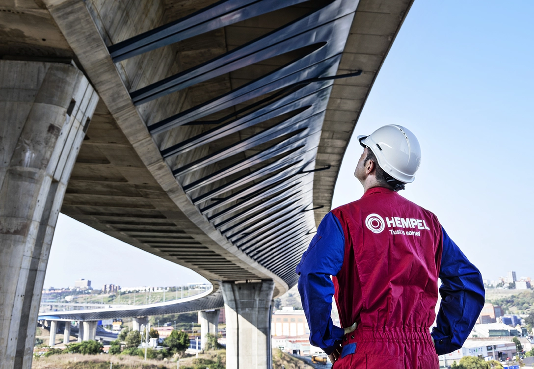 A Hempel employee in protective gear examines the underside of a large modern bridge.