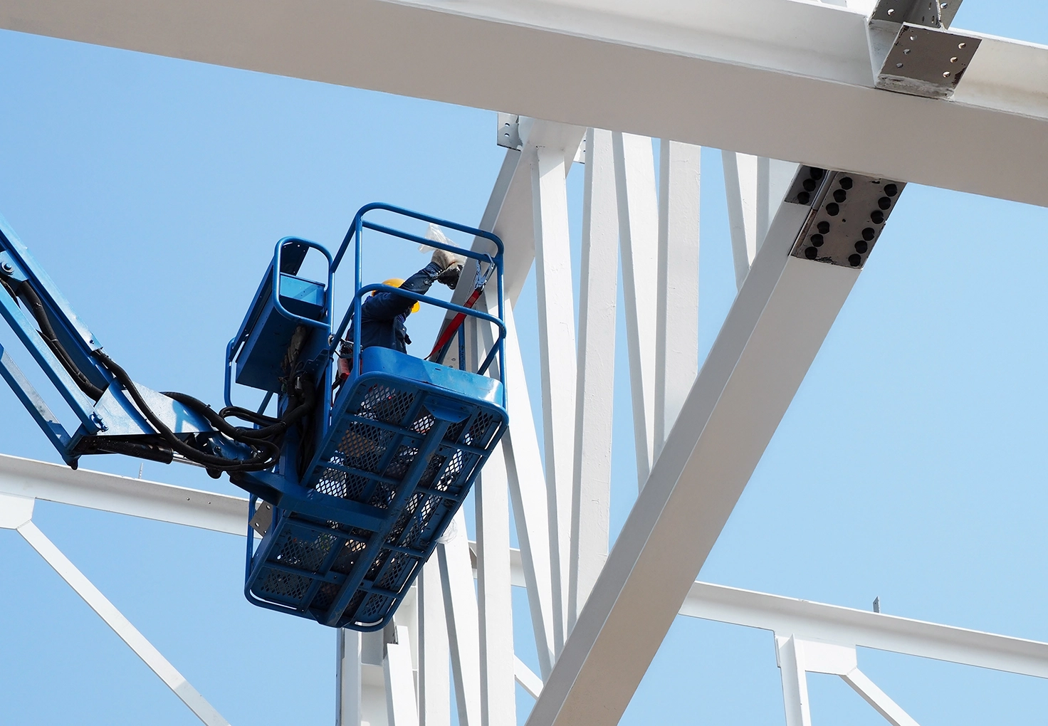 A worker in a hard hat is welding a steel structure, surrounded by scaffolding and construction materials.