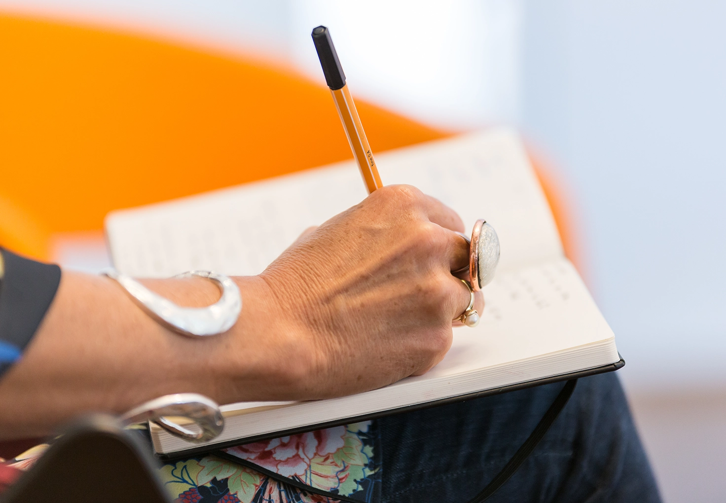 Close-up of a hand writing in a notebook with a pen, wearing a stylish bracelet.