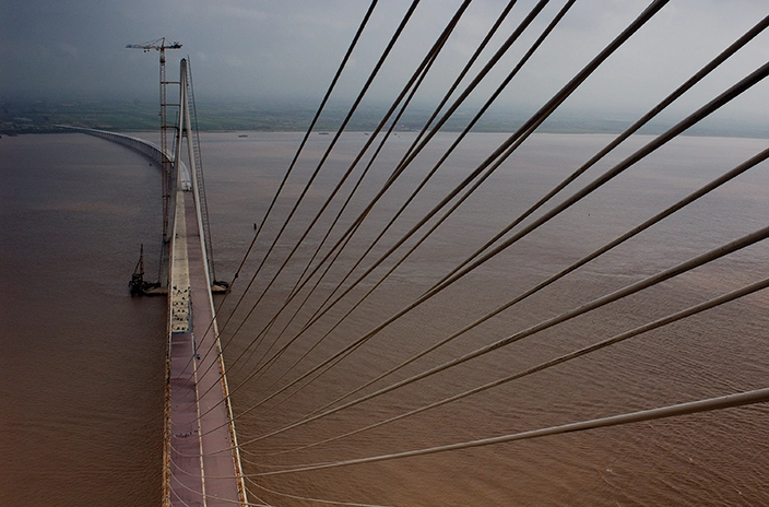 A view of a long suspension bridge with cables extending across a large body of water.