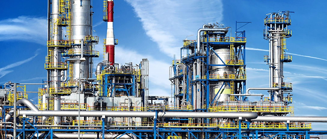 A large petrochemical plant with tall towers, pipes, and metal structures under a bright blue sky.