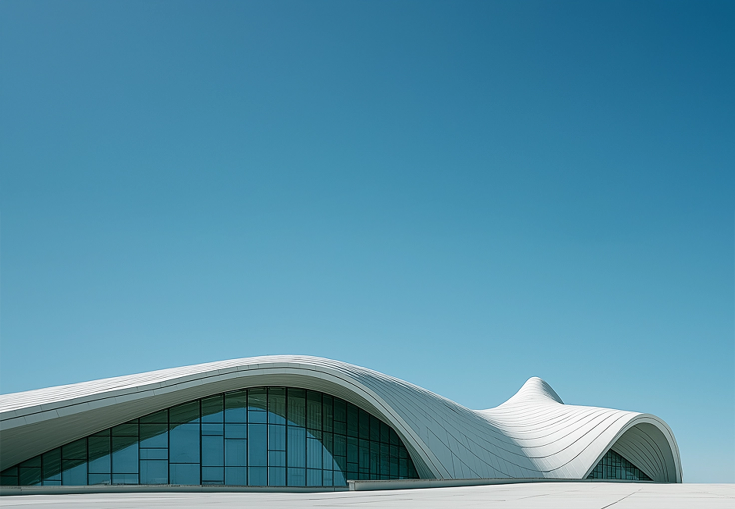 Futuristic building with smooth, flowing curves under a clear blue sky. The sleek, white exterior is contrasted by large glass windows, conveying elegance and modernity.