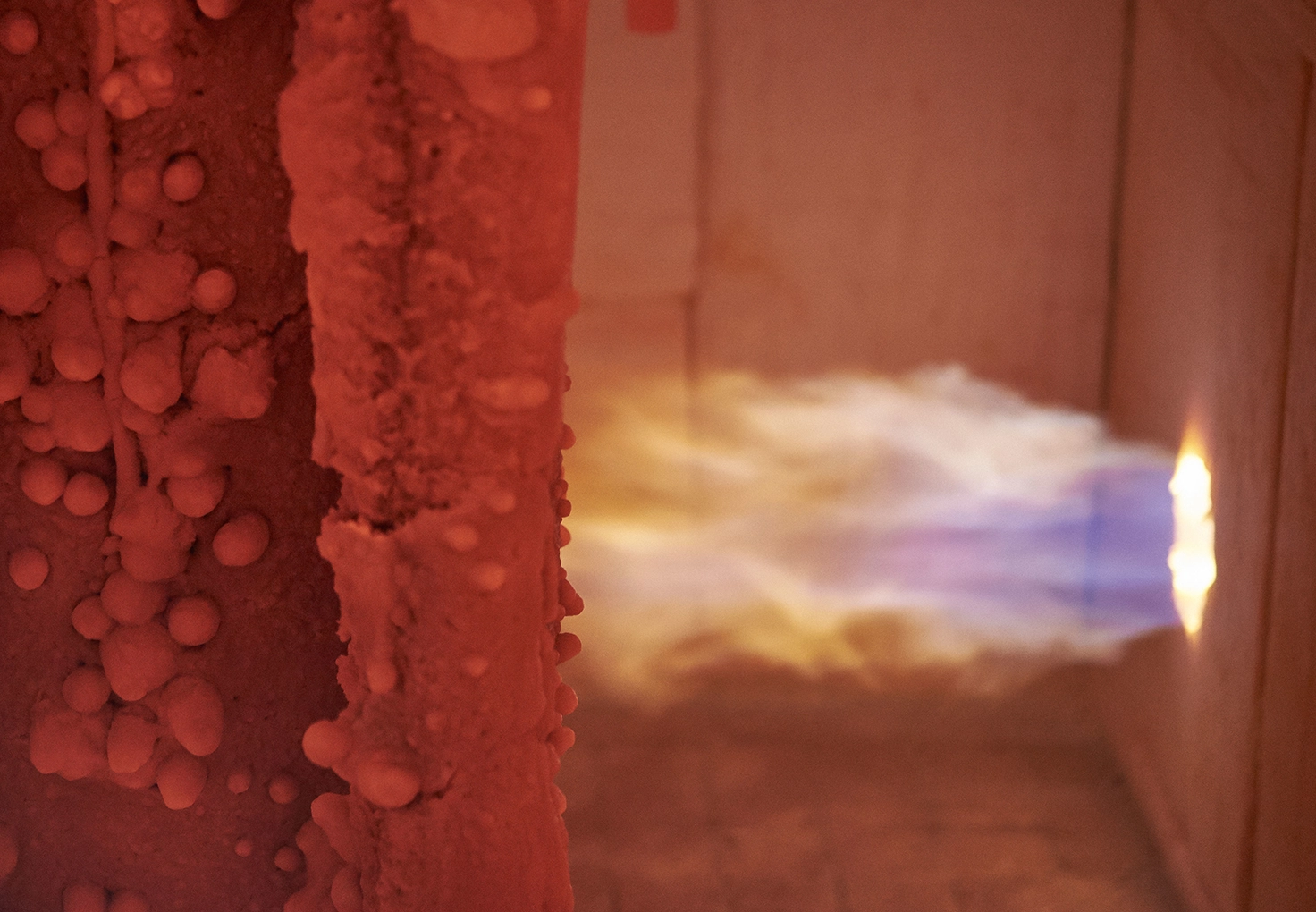 A bright blue and yellow flame inside a testing furnace, illuminating the surface of a heat-resistant material during a fire protection test.