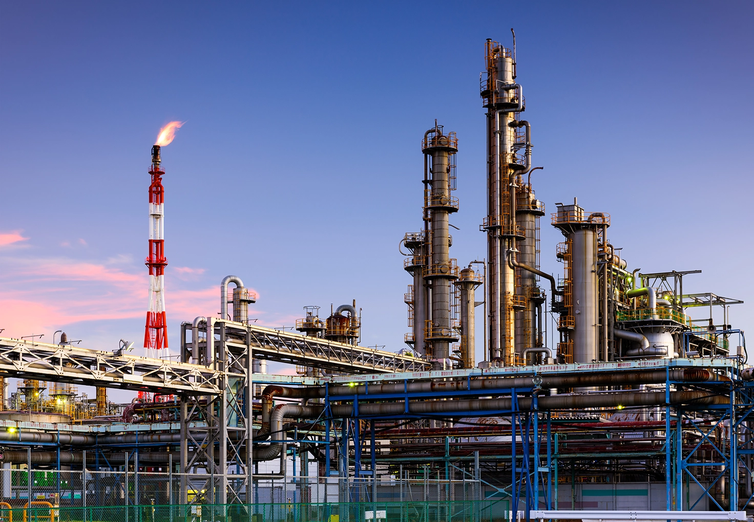 A large oil refinery featuring extensive networks of pipes and industrial structures against a clear sky.