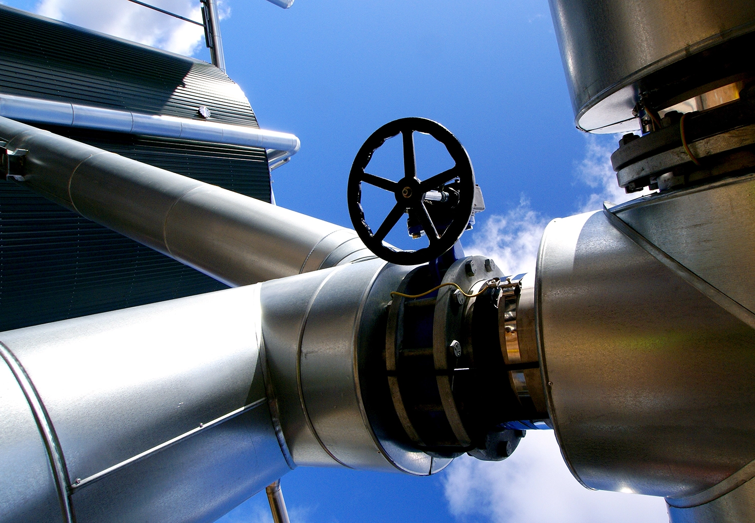Close-up of a large metallic valve on an industrial pipeline against a clear blue sky.