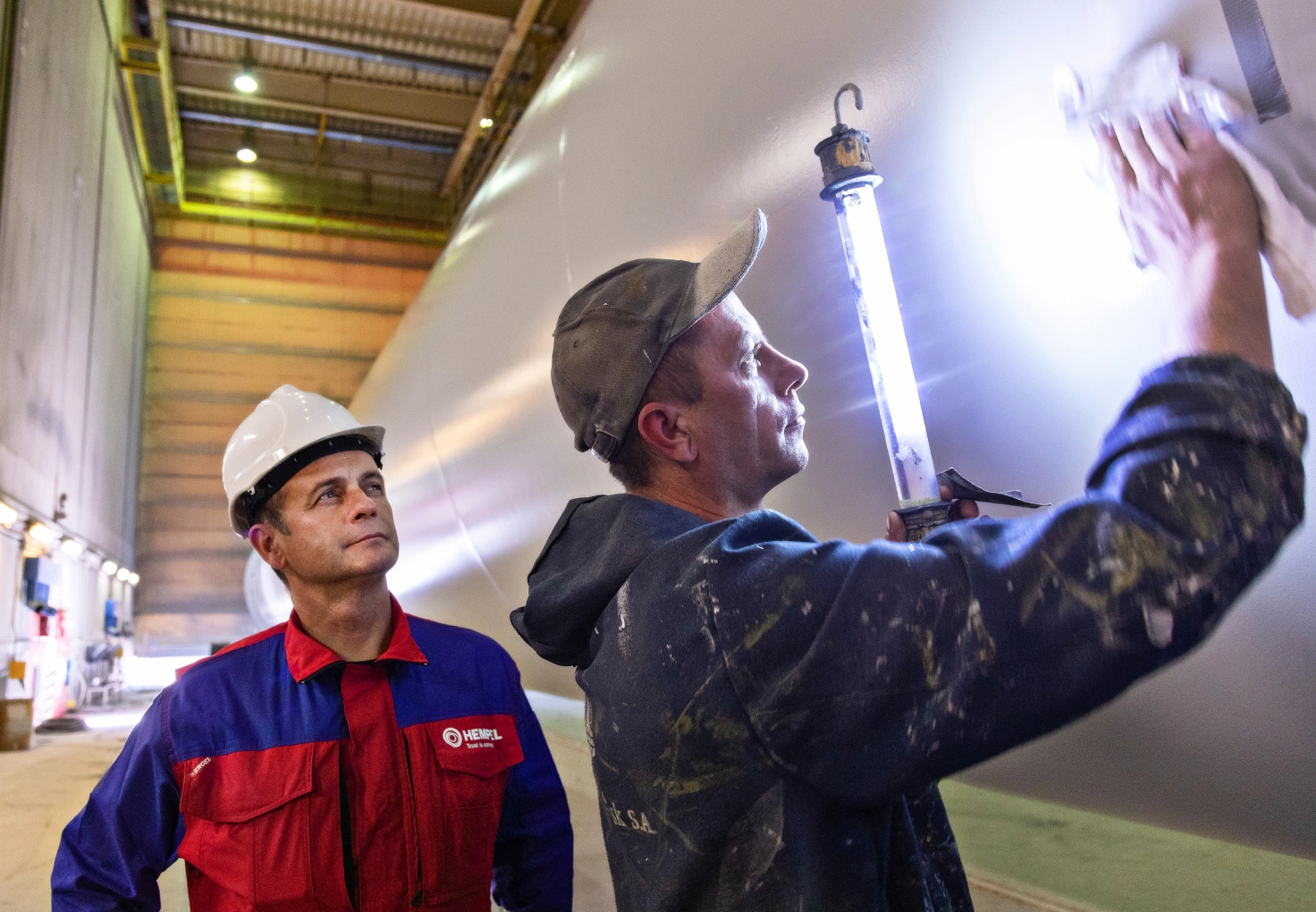  Two men in hard hats and safety glasses inspect a large turbine during maintenance work in an industrial setting.