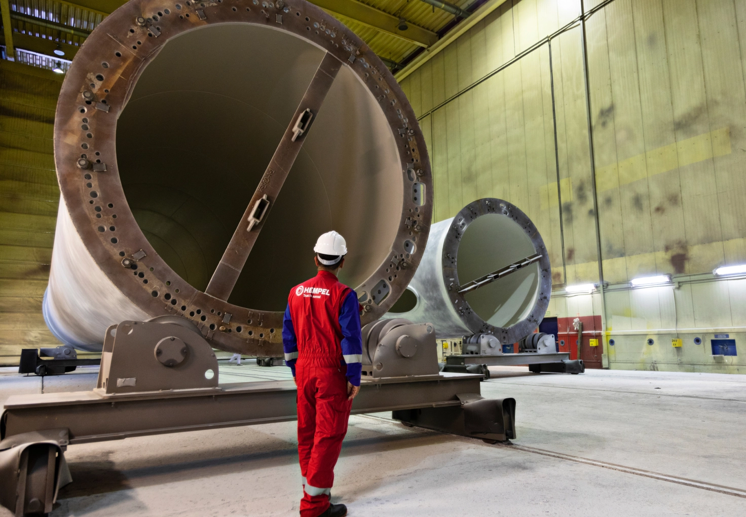  A man in a red uniform stands beside a large industrial pipe, showcasing his role in a maintenance or engineering context.