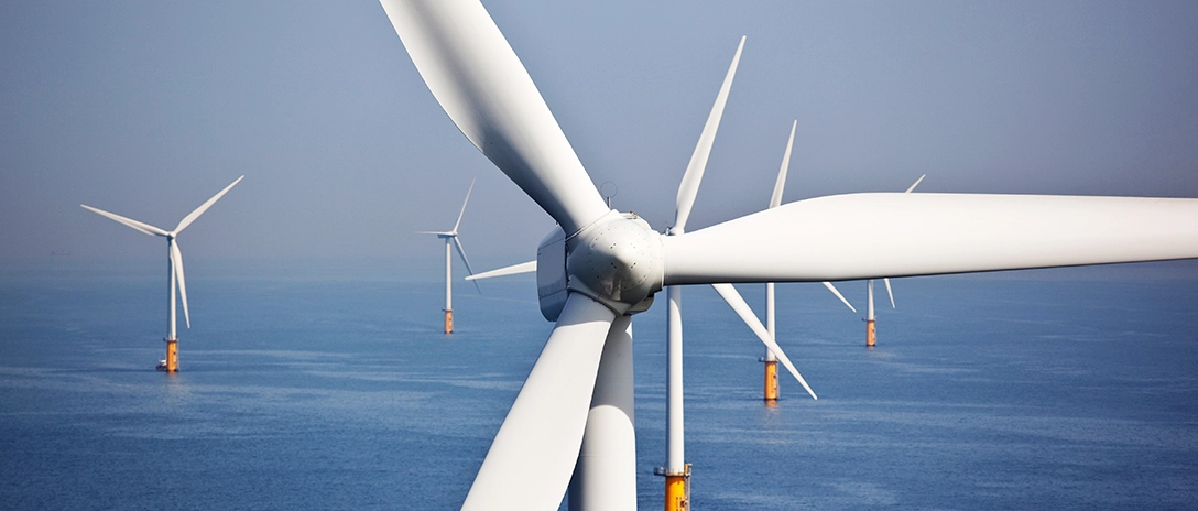 Close-up of a wind turbine blade with several offshore turbines in the background over calm water.
