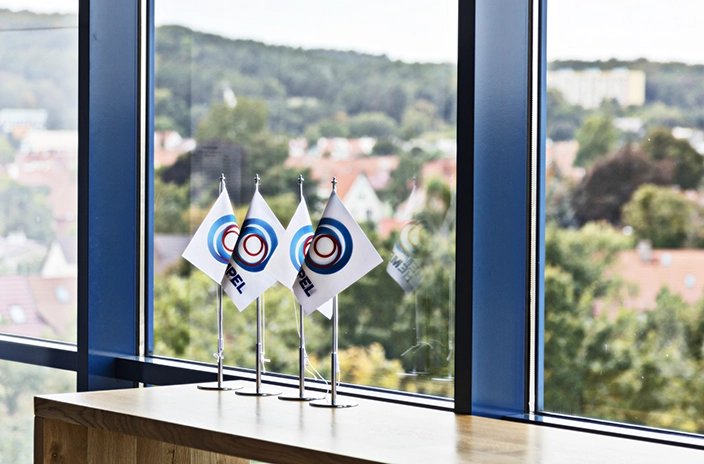 Three small Hempel flags placed on a desk by a window overlooking trees and rooftops in the background.