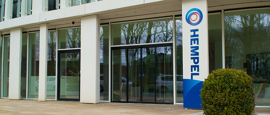 Main entrance to the Hempel headquarters, featuring glass doors and a sign with the Hempel logo on the right.