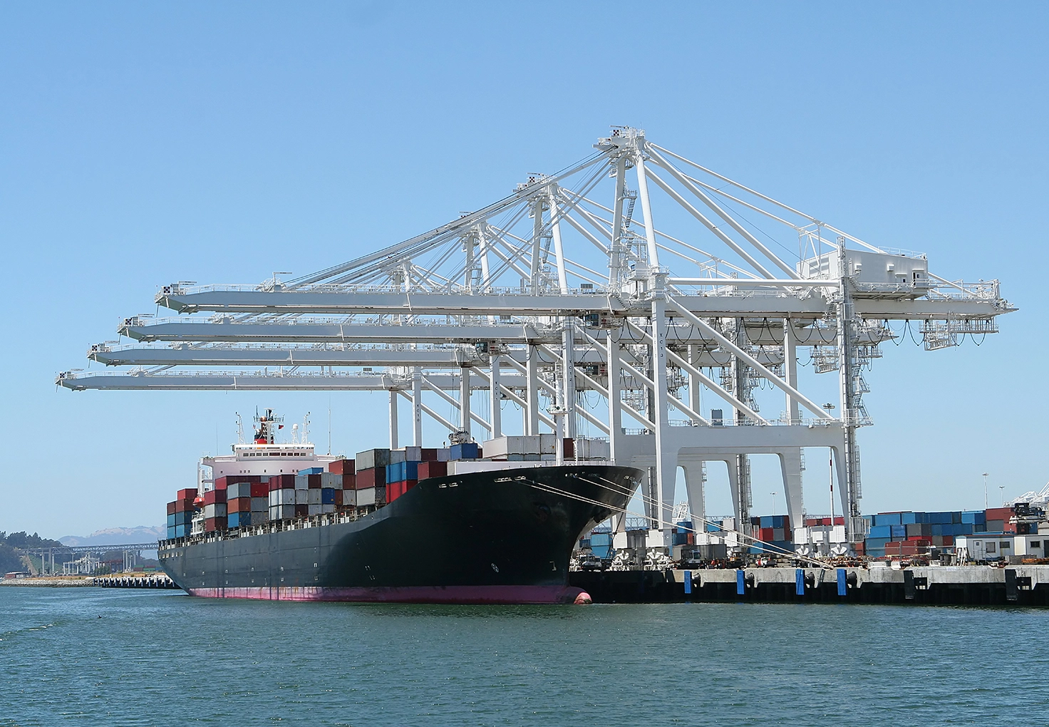 A large container ship docked at a port, surrounded by white cranes for loading and unloading.