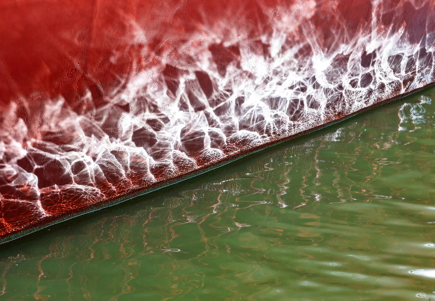 A red boat with white paint, floating on calm water, reflecting the surrounding scenery.