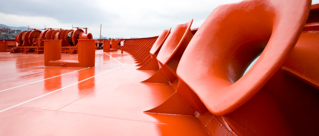 Freshly coated red fairleads along the edge of a ship's deck.