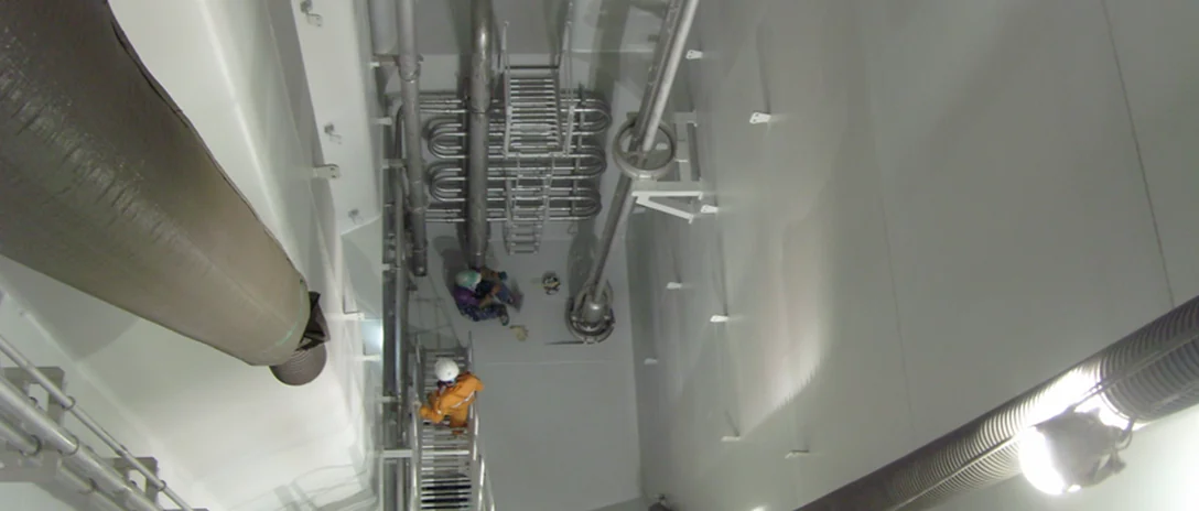View from above into a white-coated tank where two workers carry out an inspection.