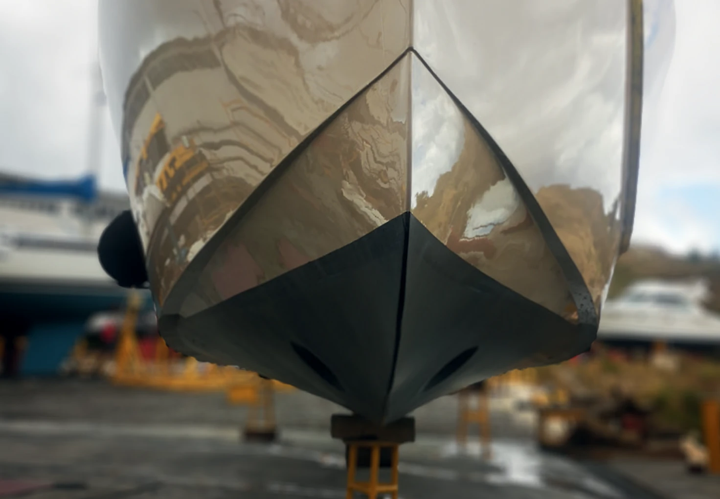 Close-up of a yacht hull with a reflective surface, showing a bow resting on supports.