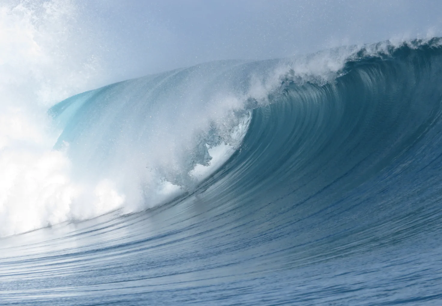 A large breaking wave captured at its peak as it curls, with water spray trailing in the air.