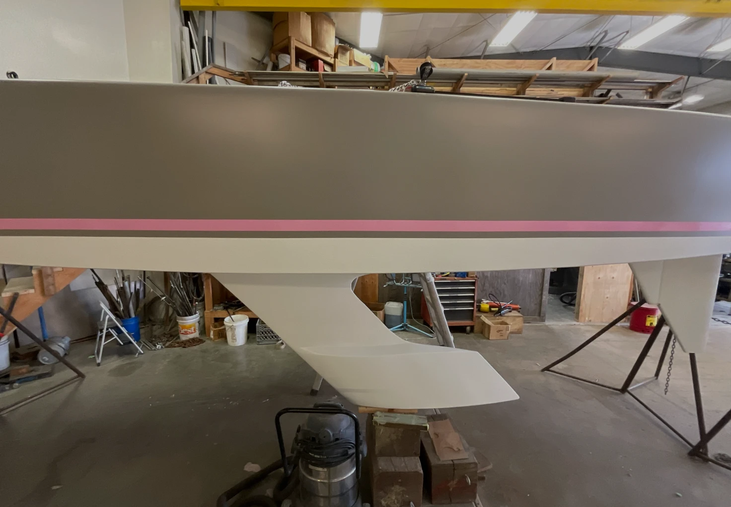 Yacht on supports in a workshop, showing a freshly painted keel with a pink stripe running along the hull.