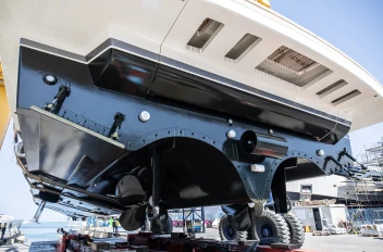 Rear view of a yacht raised on supports, focusing on the propellers and underside of the hull with a glossy black finish.
