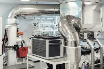 Yacht engine room with polished steel pipes and machinery, featuring ventilation and control systems.
