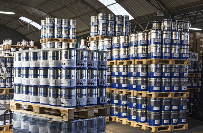 Multiple Hempel paint containers stacked on wooden pallets in a warehouse.
