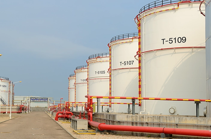 A row of white storage tanks labeled T-5105 to T-5109 with red and yellow piping in an industrial facility.
