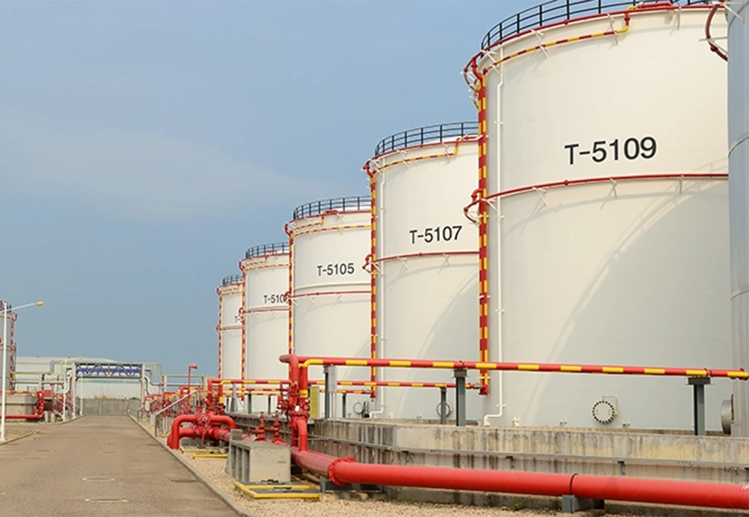 A row of white storage tanks labeled T-5105 to T-5109 with red and yellow piping in an industrial facility.