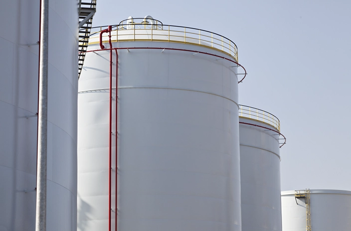 A rowof large white storage tanks with red pipes running along their sides in a storage facility.