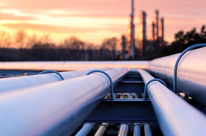 Pipelines stretching into the distance with an industrial facility visible in the background at sunset.
