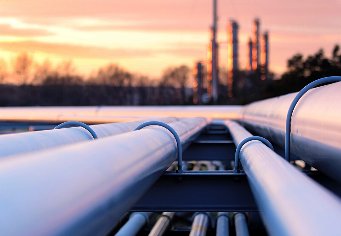 Pipelines stretching into the distance with an industrial facility visible in the background at sunset.