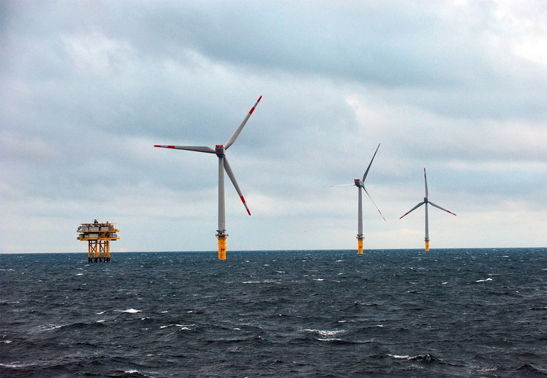 Wikinger offshore windfarm with three large wind turbines and an offshore platform in the distance on a cloudy day.