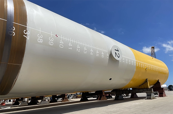 A large wind turbine foundation component coated in white and yellow, resting on supports.
