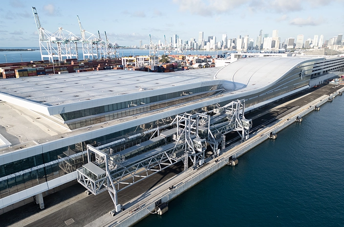 Modern cruise terminal building with passenger boarding bridges extending to a waterfront pier.