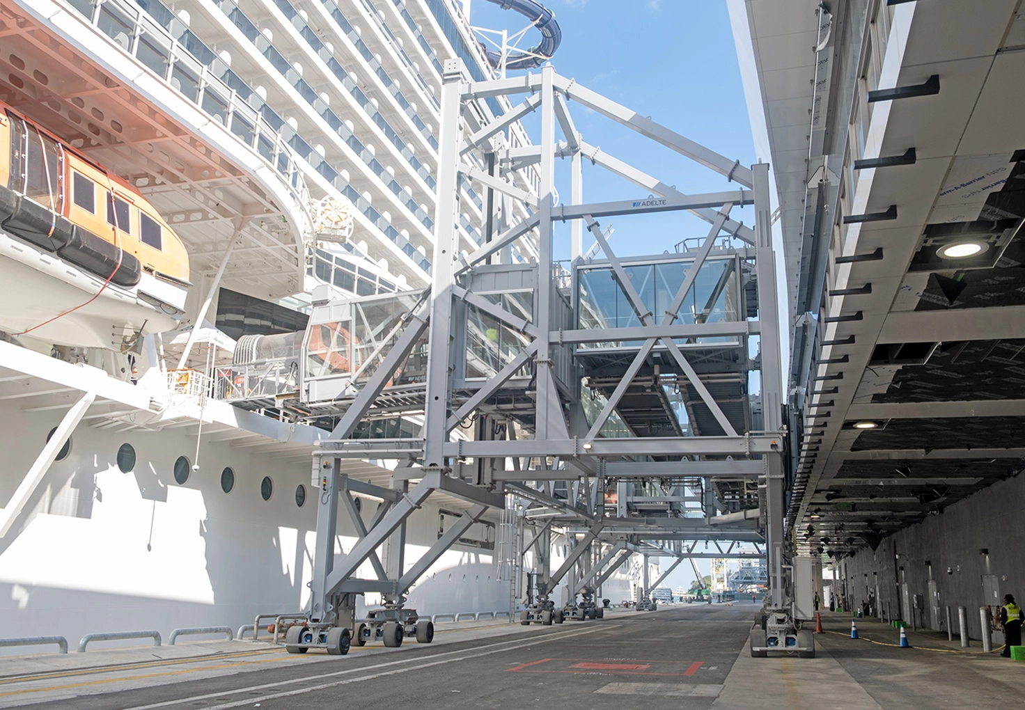Cruise ship docked at a terminal beside a covered boarding gangway connecting the ship to the pier.