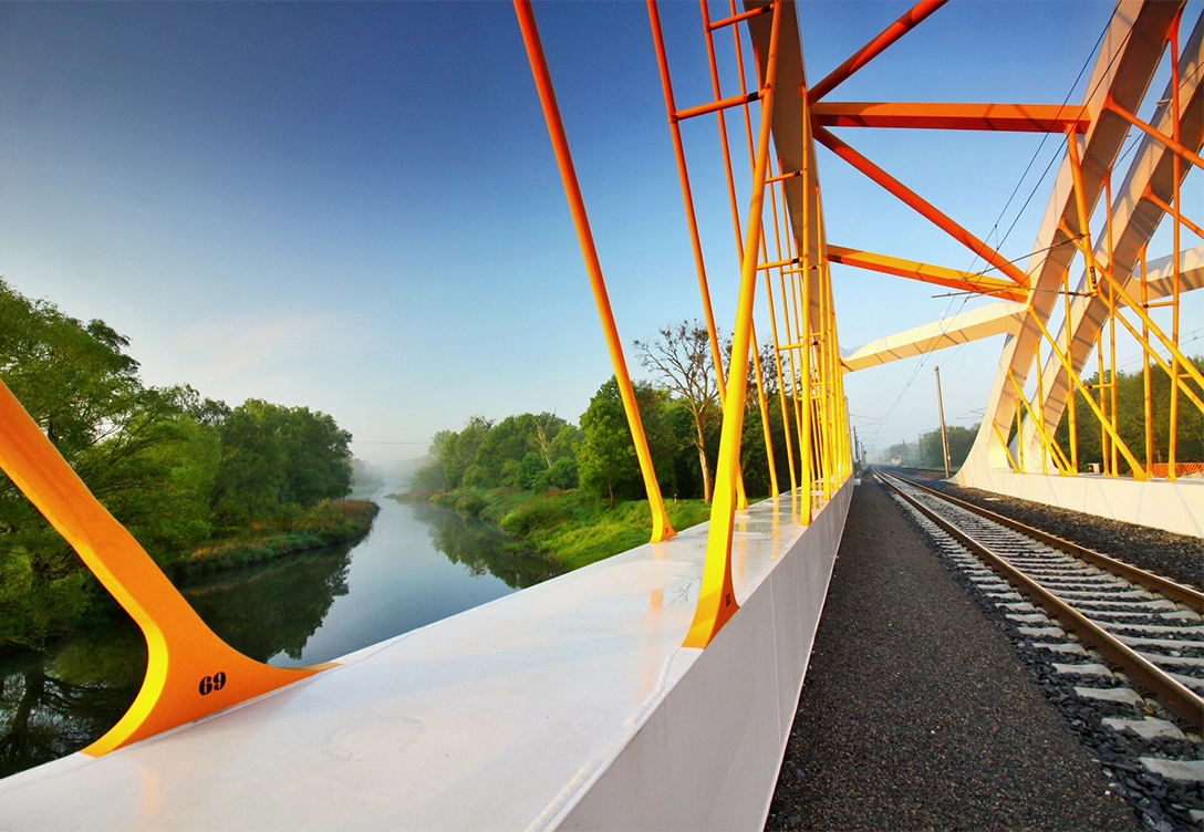 Breclav bridge with yellow-orange steel beams over a river, with railway tracks extending into the distance.