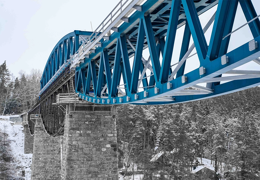 Close-up of the blue arched beams of Hracholusky Bridge, framed by a snowy winter landscape.