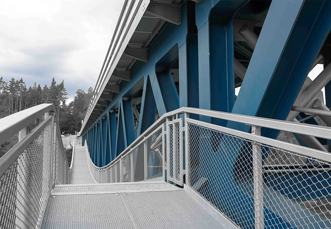 Close-up of a pedestrian metal walkway alongside the blue arched steel beams of Hracholusky Bridge.