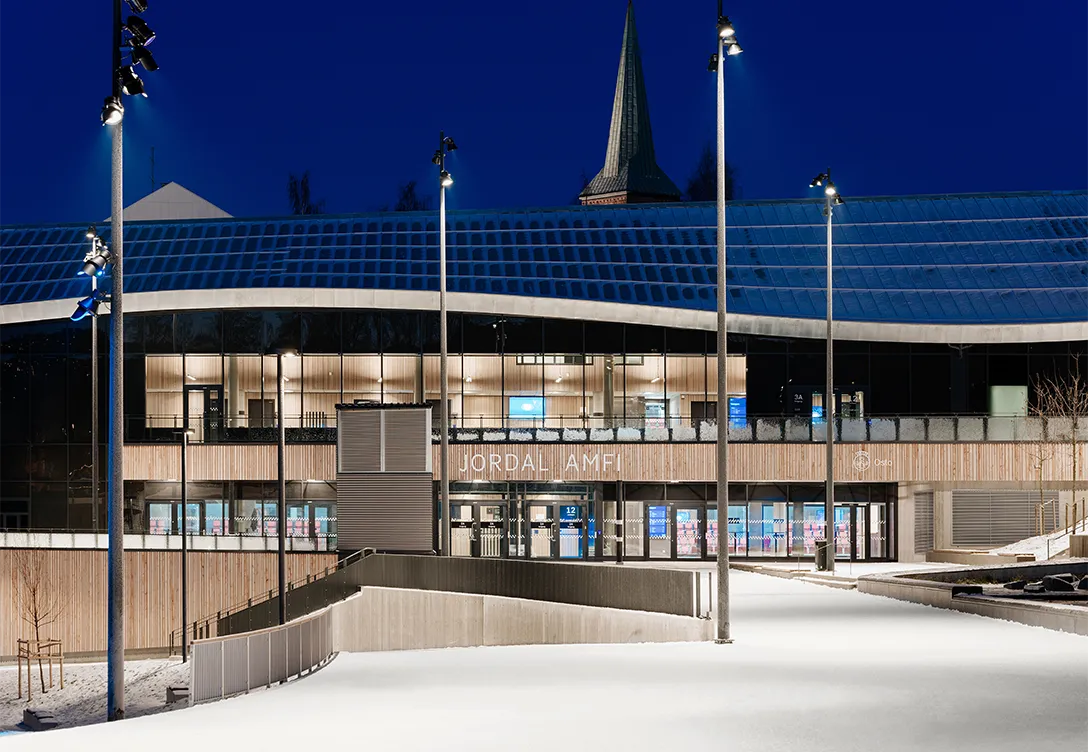 Modern exterior of Jordal Amfi stadium at night, brightly lit from the outside.