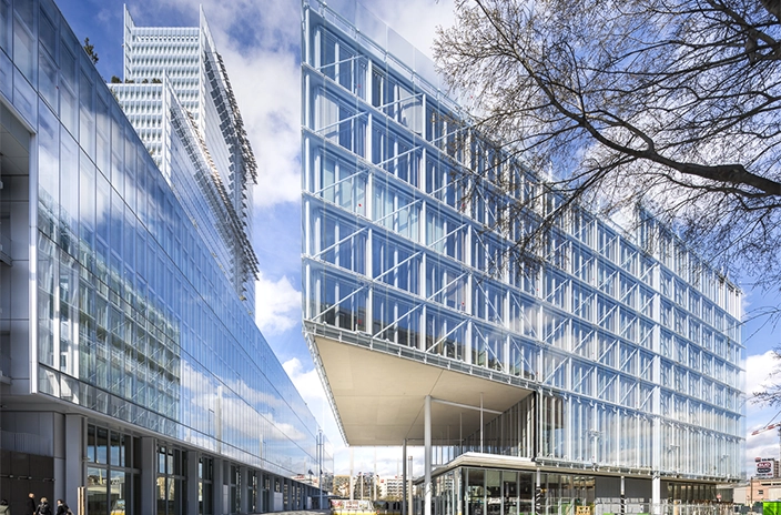 Maison de l'Ordre des Avocats, a modern glass building with sharp angles and reflective facades, set against a blue sky.