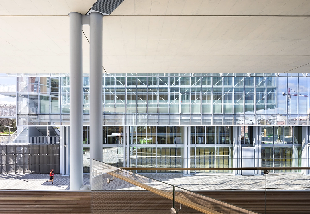 A view of the lower level of Maison de l'Ordre des Avocats, showcasing large glass panels, sleek columns, and a modern staircase.