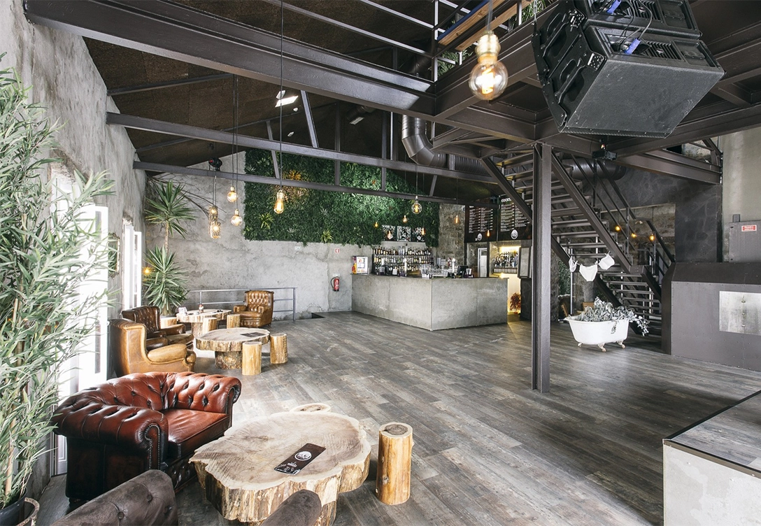 Rustic interior of Raiz cocktail bar with leather chairs, wooden tables, an industrial-style bar, plant wall, and exposed beams.