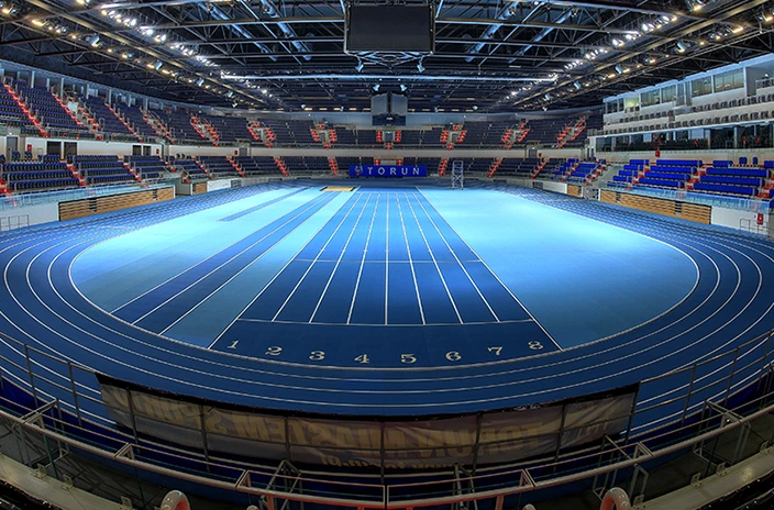Indoor view of Torun sports stadium featuring a blue running track surrounded by spectator seating.