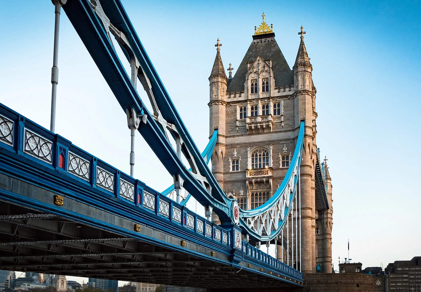 Close-up of London's Tower Bridge, showcasing its blue suspension cables and ornate details against a clear sky.