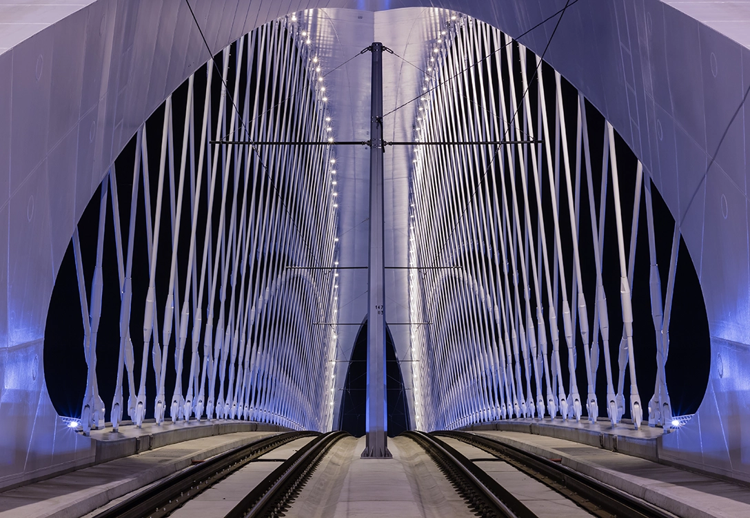 A nighttime view of Troja Bridge, illuminated by lights along its structure, with the symmetrical crisscrossing cables and railway tracks.